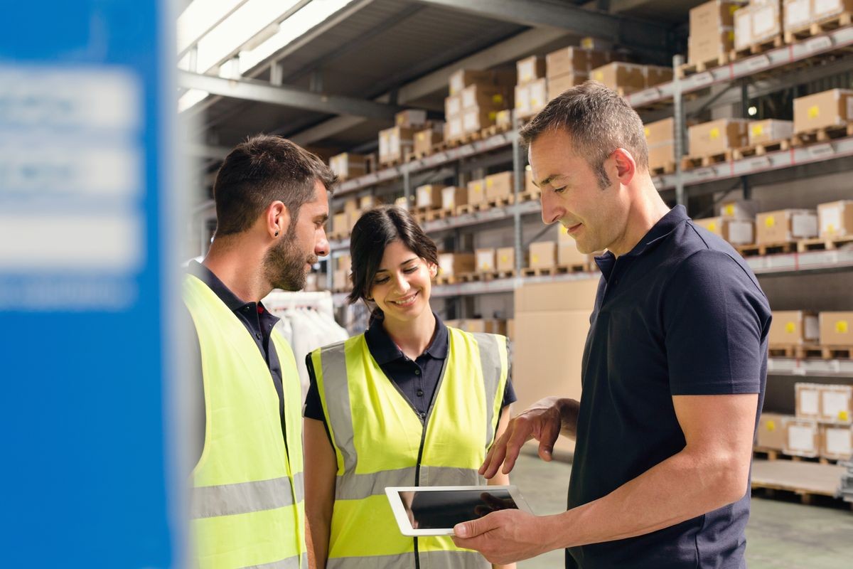 Supervisor instructing warehouse workers using digital tablet in distribution warehouse